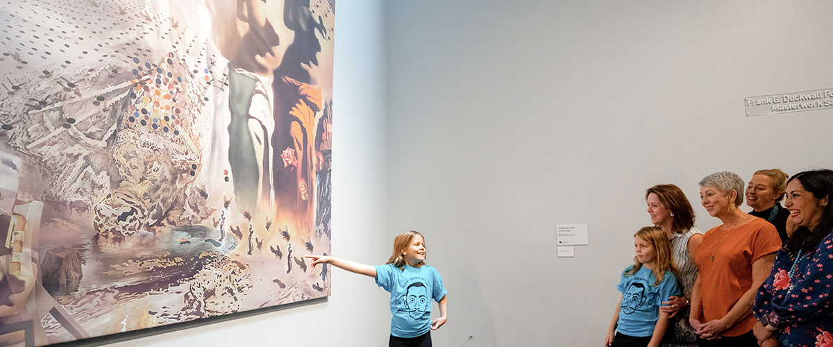 child points at art in front of eager crowd