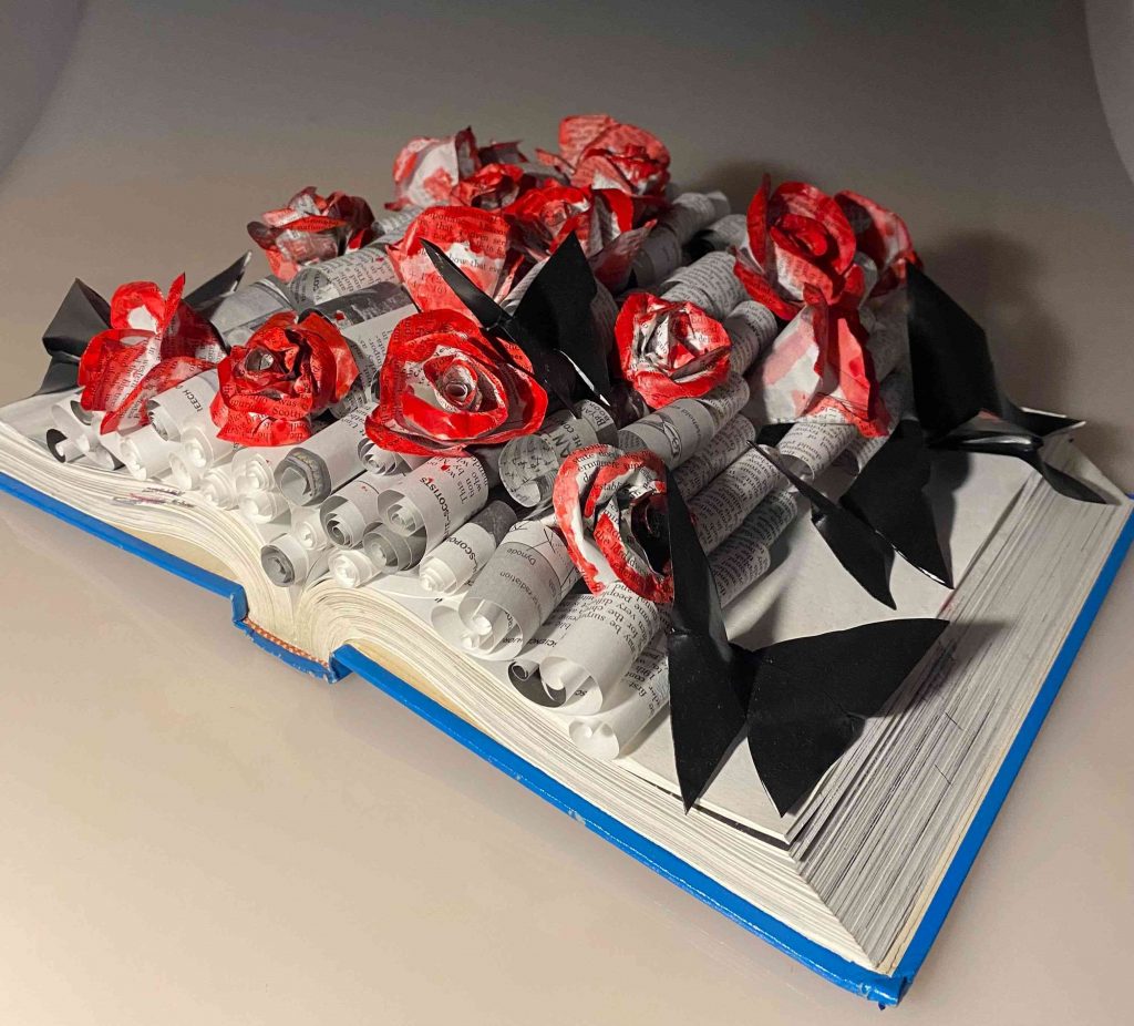 An open book with rolled papers on it, covered by roses