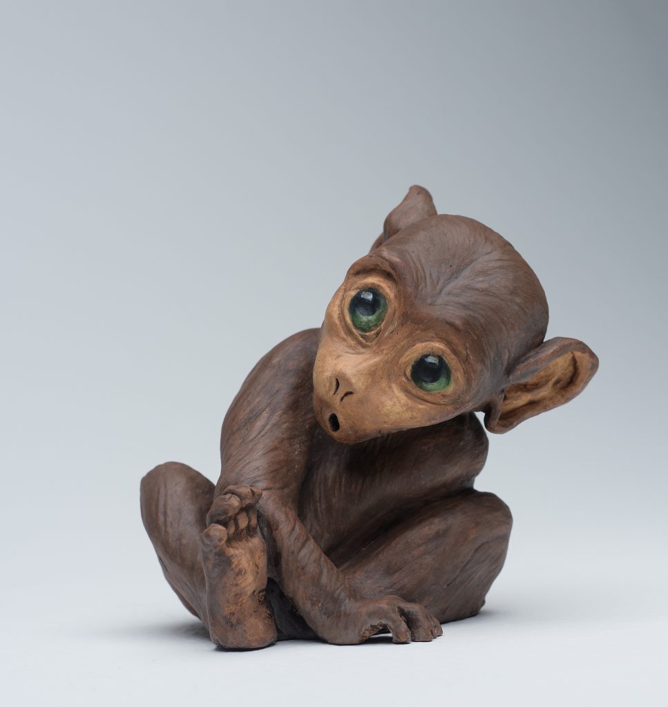 a small brown wooden monkey with green eyes

