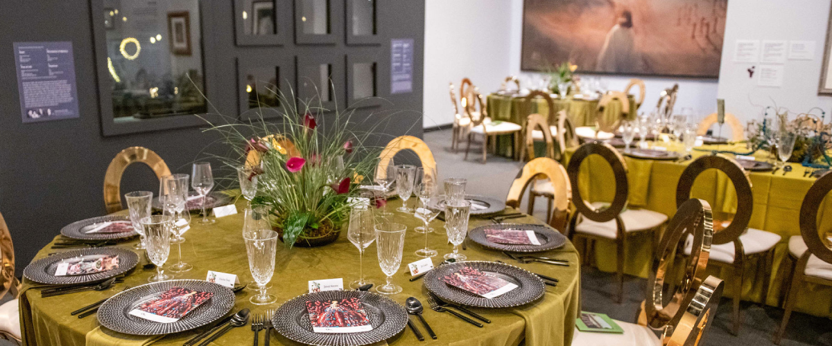 Formal dinner tables set inside The Dalí Museum galleries with green linens, gold chairs, floral centerpieces and elegant place settings.